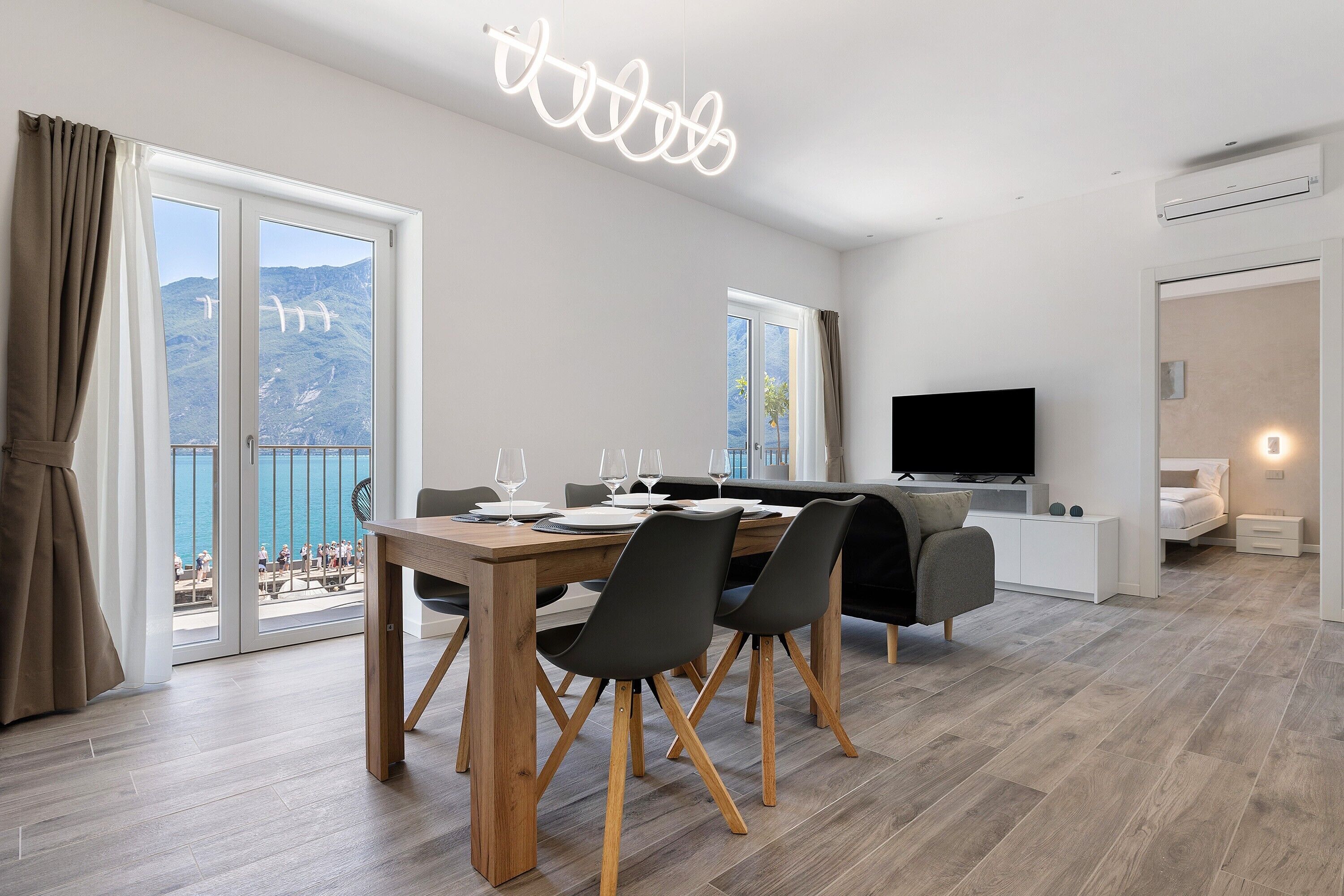Ein modernes Wohnzimmer mit Essbereich, einem Flachbildfernseher und einem Balkon mit Meerblick.