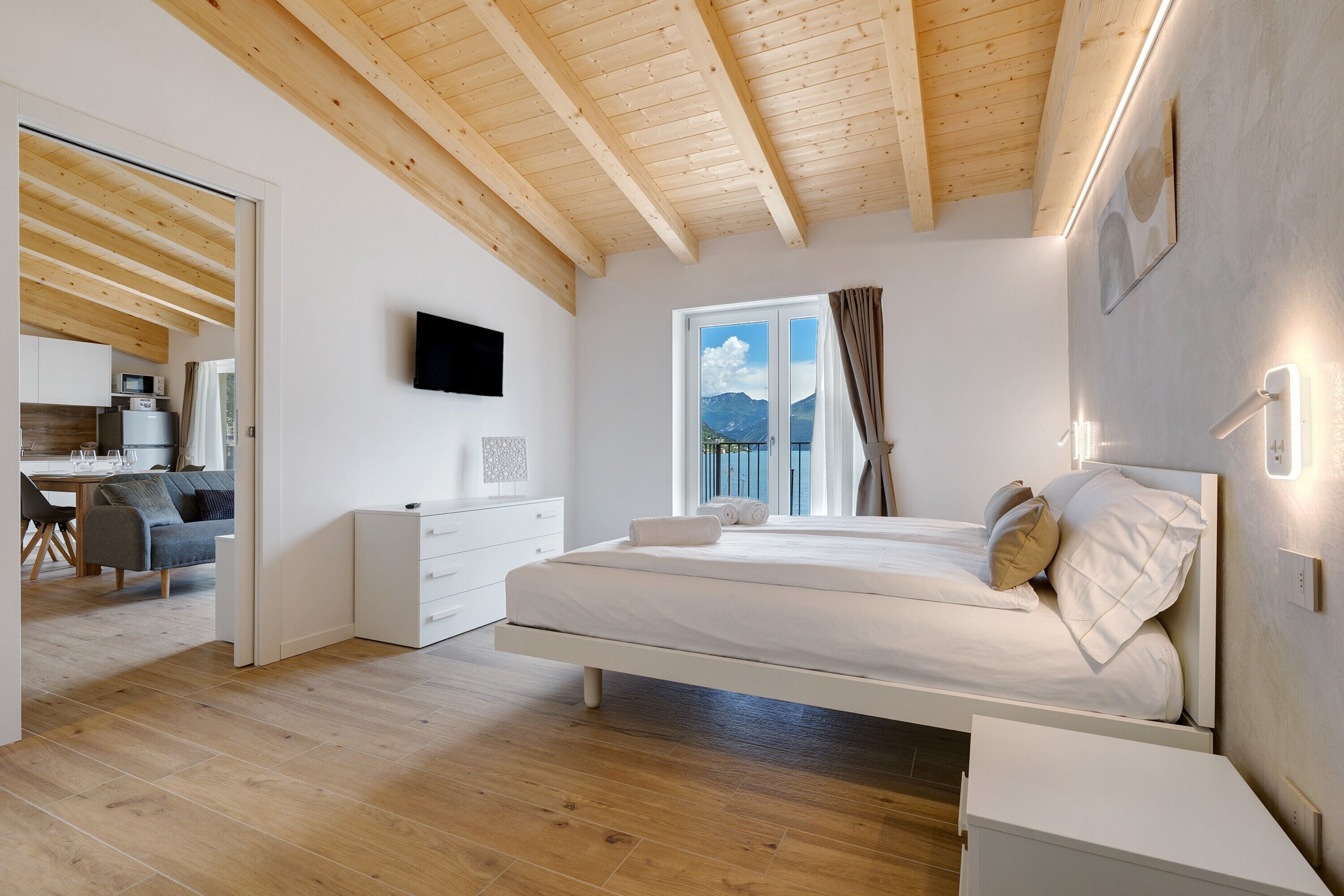 Un dormitorio con techo de madera, una cama, una mesita de noche y un televisor, con una ventana que ofrece vistas a la montaña.