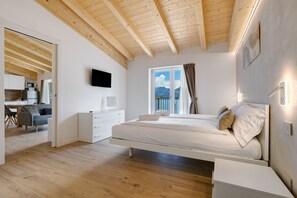 Un dormitorio con techo de madera, una cama, una mesita de noche y un televisor, con una ventana que ofrece vistas a la montaña.