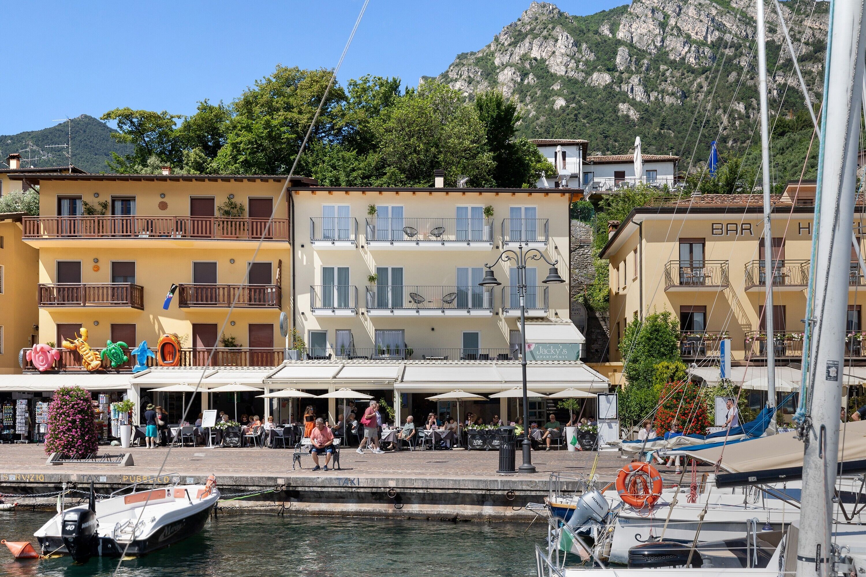 Un edificio frente al agua con balcones, asientos exteriores y un puerto deportivo con barcos.