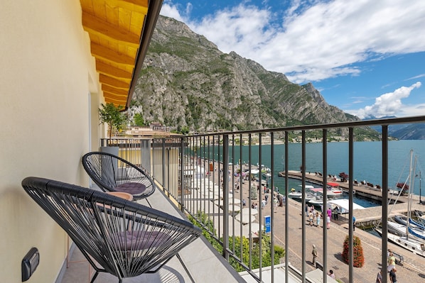 A balcony with two black chairs, a wooden ceiling, and a view of a marina with boats and mountains in the background.