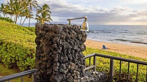 Une structure rocheuse surmontée d’un robinet métallique, une plage bordée de palmiers et une rambarde.