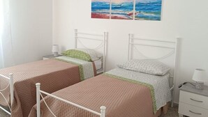 Een slaapkamer met twee eenpersoonsbedden, een nachtkastje, een lamp en een schilderij van een zonsondergang boven de oceaan.