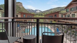 A balcony with a view of a swimming pool, lounge chairs, and a mountainous landscape.