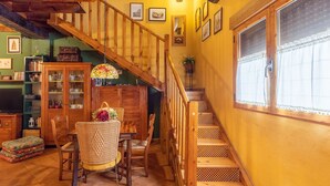 A wooden staircase with a patterned railing, a dining area with wicker chairs and a table, and a bookshelf filled with books and decorative items.