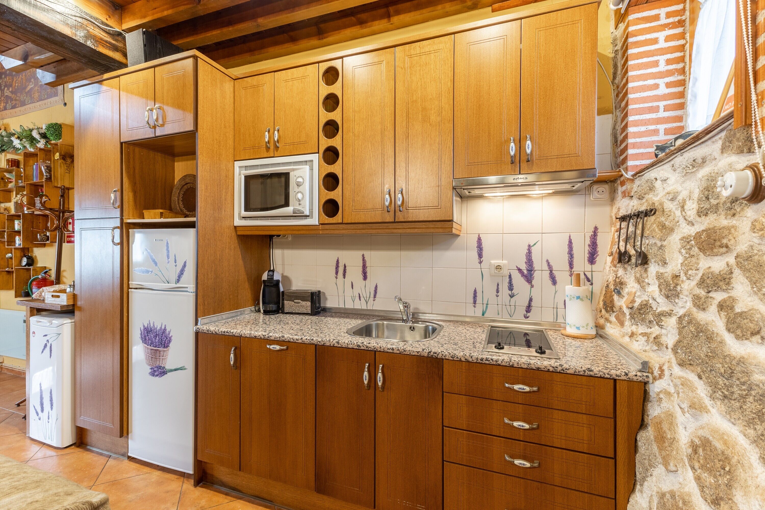 A kitchen with wooden cabinets, a granite countertop, a built-in microwave, and a stone wall.