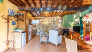 A rustic interior with exposed wooden beams, a stone wall, a fireplace, and a dining area with a wooden table and chairs.
