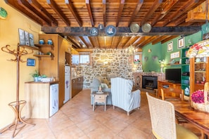 A rustic interior with exposed wooden beams, a stone wall, a fireplace, and a dining area with a wooden table and chairs.