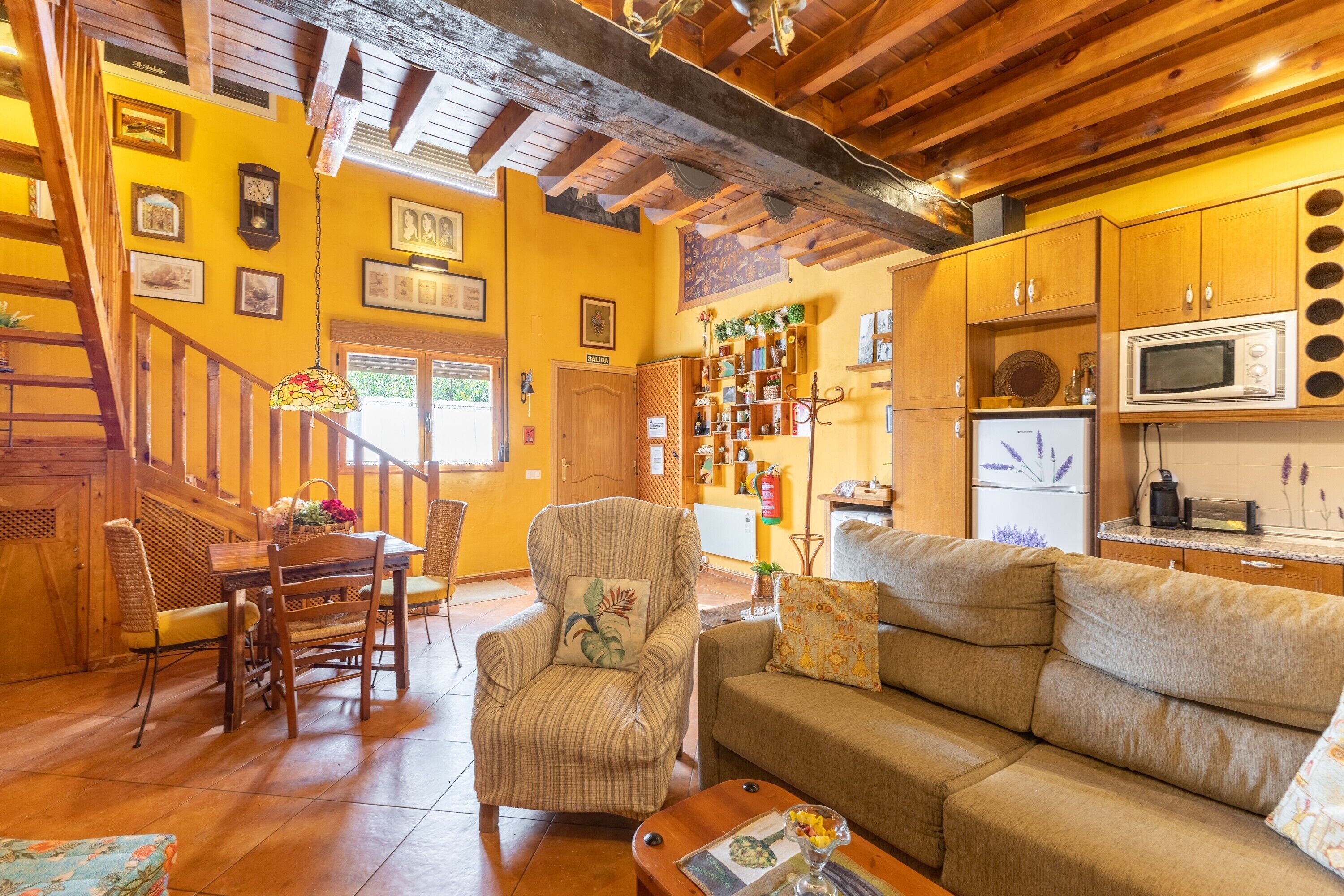 Una sala de estar acogedora con una escalera de madera, un comedor y una cocina con armarios de madera y un microondas.