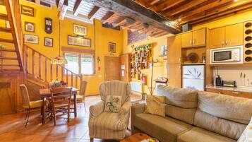 Una sala de estar acogedora con una escalera de madera, un comedor y una cocina con armarios de madera y un microondas.