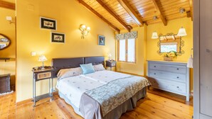 A bedroom with a wooden ceiling, a bed with a headboard, bedside tables, a dresser, and wall-mounted lamps.