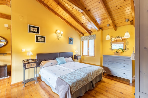 A bedroom with a wooden ceiling, a bed with a headboard, bedside tables, a dresser, and wall-mounted lamps.