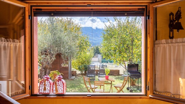 A room with a large window overlooking a backyard with a grill and patio furniture.