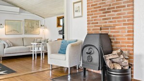 A cozy living room with a fireplace, a sofa, a coffee table, and framed artwork on the walls. - 4 bedroom stunning home in Gilleleje (Gilleleje)