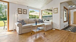 A spacious living room with a large window, a sofa, a coffee table, and a door leading to an outdoor area. - 4 bedroom stunning home in Gilleleje (Gilleleje)