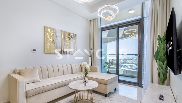 Un salon moderne avec un canapé beige, une table basse ronde et une grande fenêtre donnant sur la ville.