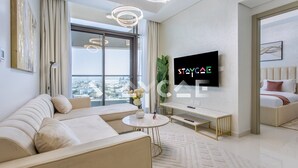 Un salon moderne comprenant un canapé, une table basse, un téléviseur fixé au mur et une grande fenêtre donnant sur la ville.