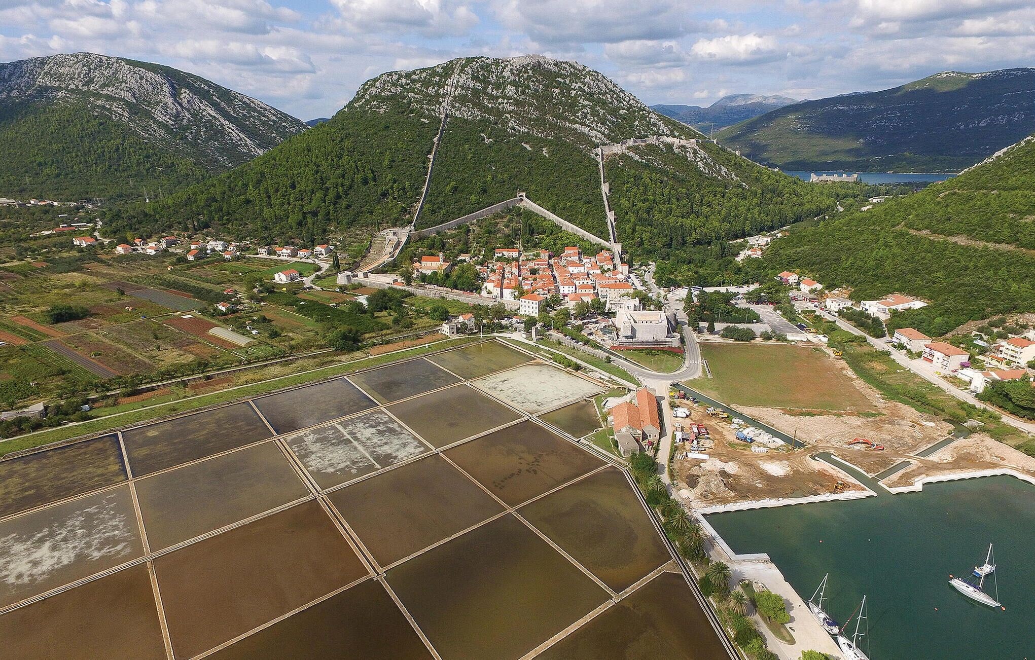 An aerial view of a coastal town with terraced fields, a fortified structure, and a marina.
