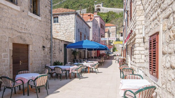 Une rue étroite avec des tables en terrasse, des bâtiments en pierre et une enseigne de restaurant.
