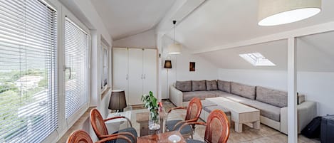 Una sala de estar moderna con una mesa de comedor de vidrio, sillas de mimbre, un sofá y un ventanal con persianas.