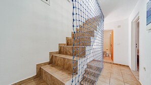 Un escalier muni d’une barrière de sécurité en filet bleu, menant à une pièce où se trouvent des toilettes et une douche.