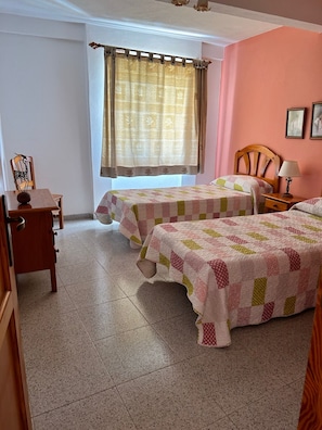 A room with two beds, a wooden chair, a small table, and a window with curtains.