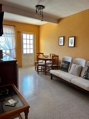 A living room with a sofa, dining table, chairs, a TV, and a ceiling light fixture.