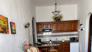 A living room with wicker furniture, a dining area, and a kitchen with wooden cabinets. - Apartment 'Apartamento 4' with Shared Pool, Private Terrace, and Wi-Fi (Los Llanos)