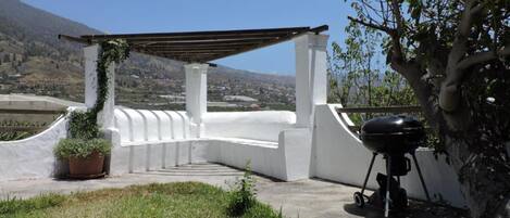 A covered outdoor area with a barbecue grill, white walls, and a view of a valley.