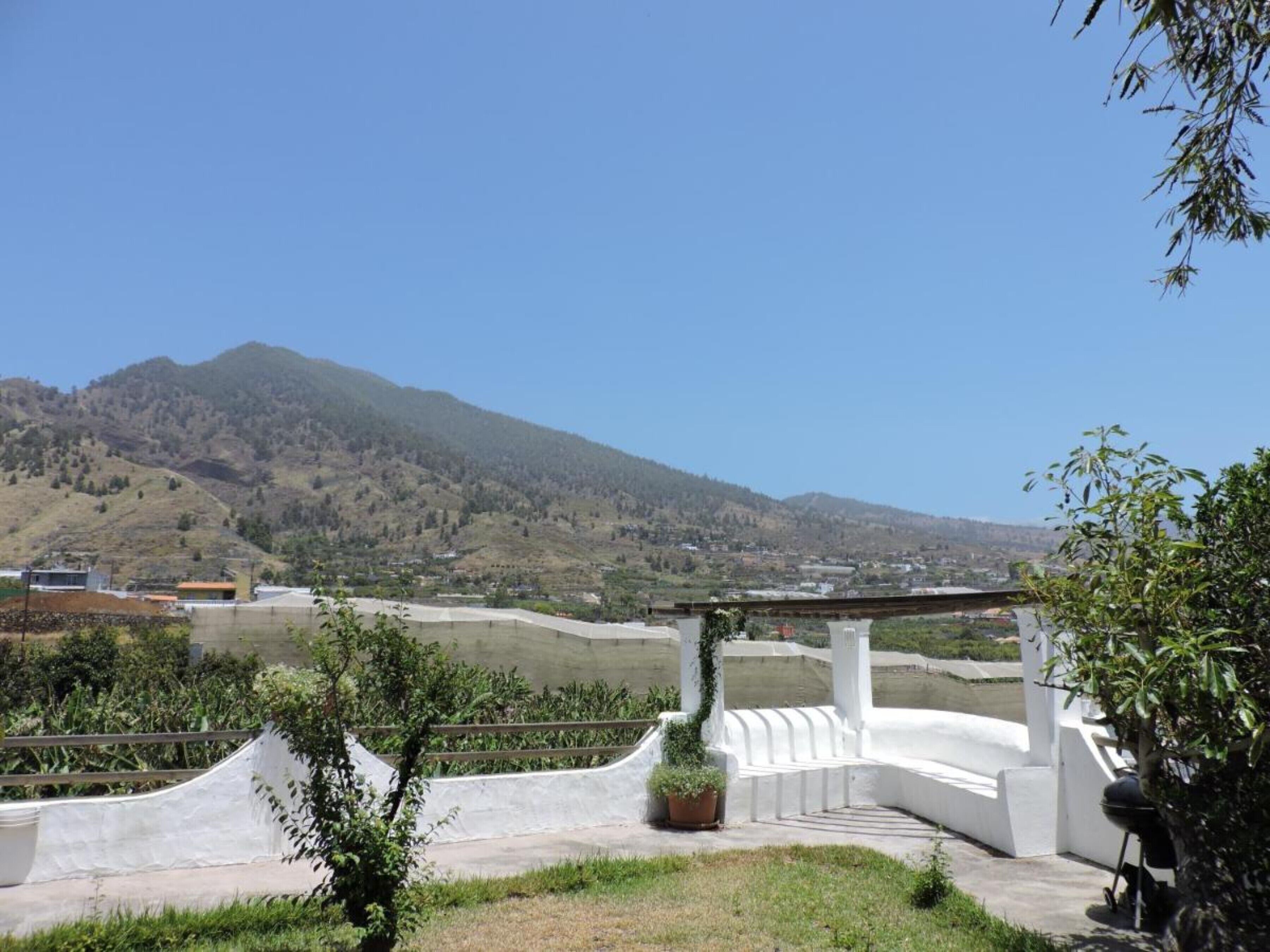 A white building with a curved roof, surrounded by greenery and a mountainous landscape.