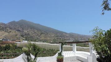 A white building with a curved roof, surrounded by greenery and a mountainous landscape.