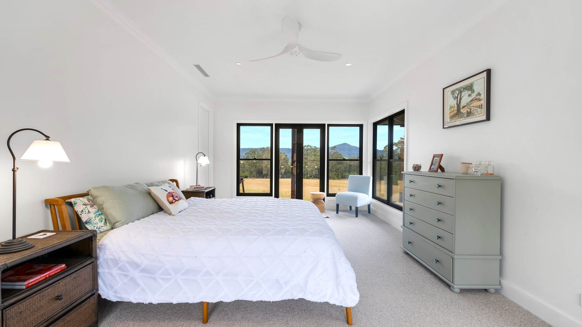 A bedroom with a large bed, a dresser, a chair, and a desk with a lamp.