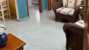 Une pièce comprenant un lit, une chaise en osier, une table en bois et une porte donnant sur une autre pièce.