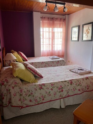 Une chambre avec deux lits, un plafond en bois, une fenêtre avec des rideaux et des tableaux encadrés accrochés au mur.