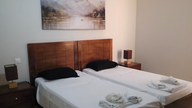 A double bed with white linens, two black pillows, and a wooden headboard. There are two bedside tables, one with a lamp and the other with a speaker. A painting of birds and water is on the wall above the bed. - Villa sérénité, Yasmine hamamet (Yasmine Hammamet)