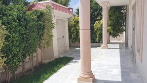 A covered outdoor area with a tiled floor, columns, and a small garden with grass and trees. - Villa sérénité, Yasmine hamamet (Yasmine Hammamet)