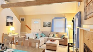 A cozy living room with a sofa, a coffee table, and a dining area with chairs and a table. - Charming Cape Cod summer house conveniently located  with plenty to offer. (Mashpee)
