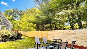 A patio area with outdoor seating and a wooden fence. - Charming Cape Cod summer house conveniently located  with plenty to offer. (Mashpee)