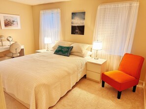 Una habitación de hotel ordenada con una cama grande, dos mesitas de noche con lámparas, una silla y un cuadro en la pared.