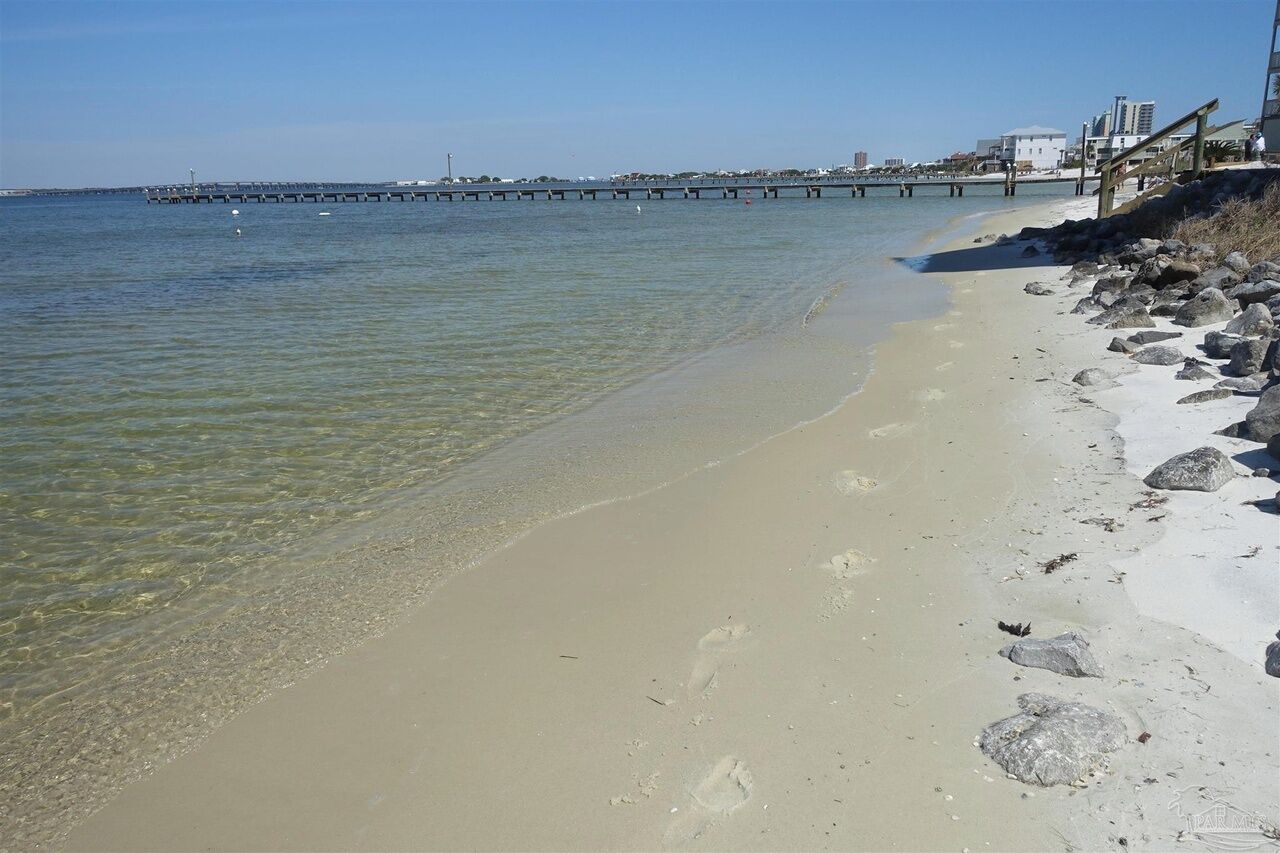 A beach with clear water, a wooden pier, and a rocky shoreline.
