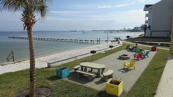 A beachside patio with a concrete table and benches, colorful chairs, and planters.