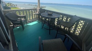 A balcony with a view of the sea, furnished with wicker chairs and a round table. - New, update, waterfront condo. Relaxing water sounds and view. (Pensacola Beach)