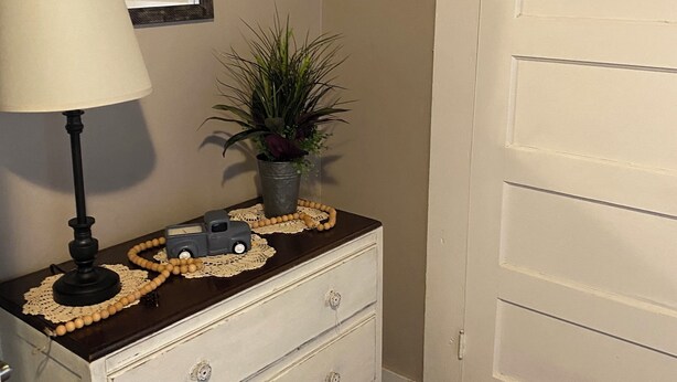 A hallway with a white dresser, a lamp, a potted plant, and a door.