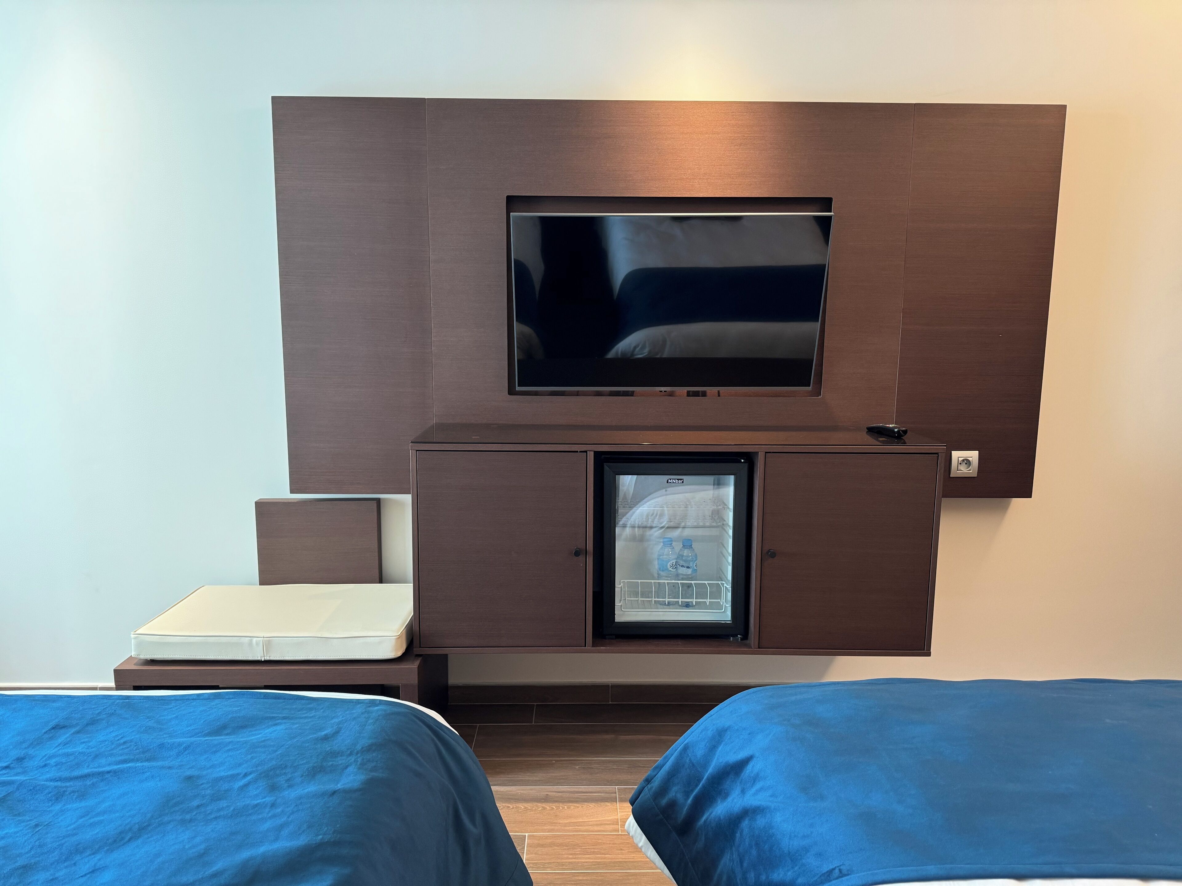 Una habitación de hotel con cama, televisión en mueble de madera y minibar.