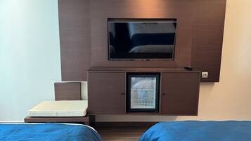 Une chambre d’hôtel avec un lit, un téléviseur fixé à un meuble en bois et un mini-bar.