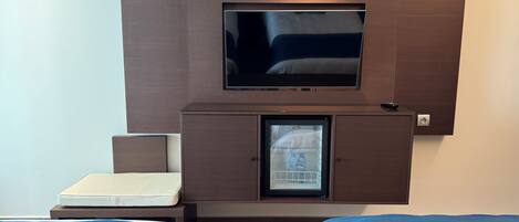Una habitación de hotel con cama, televisión en mueble de madera y minibar.