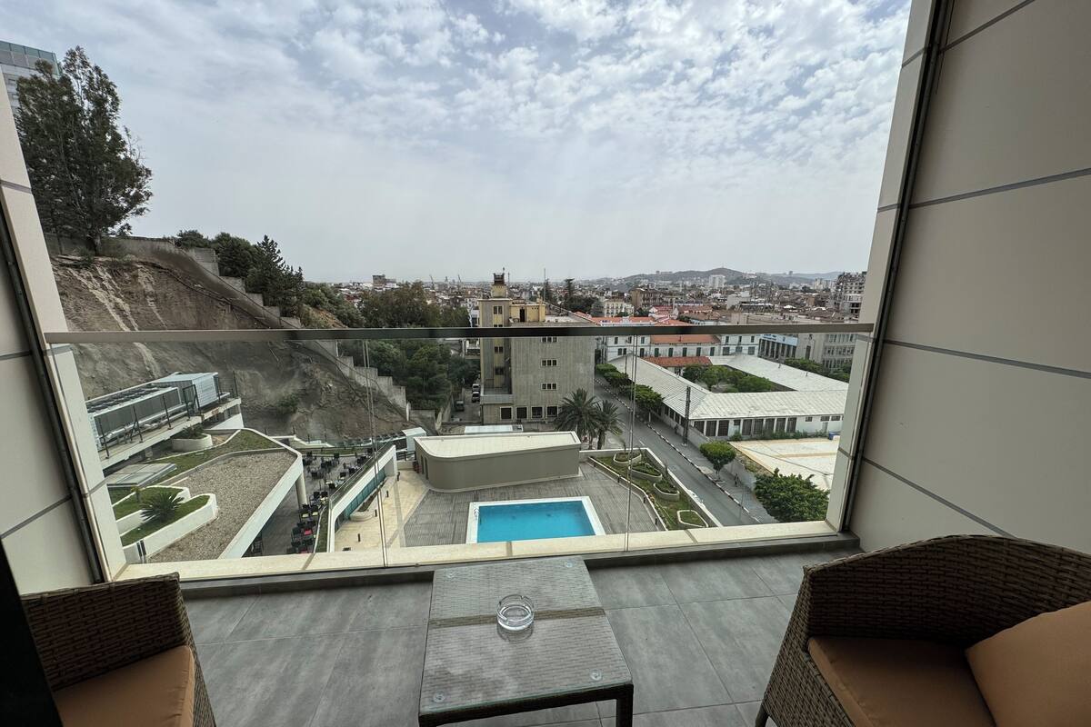 A balcony with a view of a swimming pool, cityscape, and modern buildings.