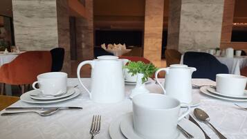 Una mesa de comedor dispuesta con vajilla blanca, incluyendo tazas, platillos, una tetera y un pequeño florero con una planta.