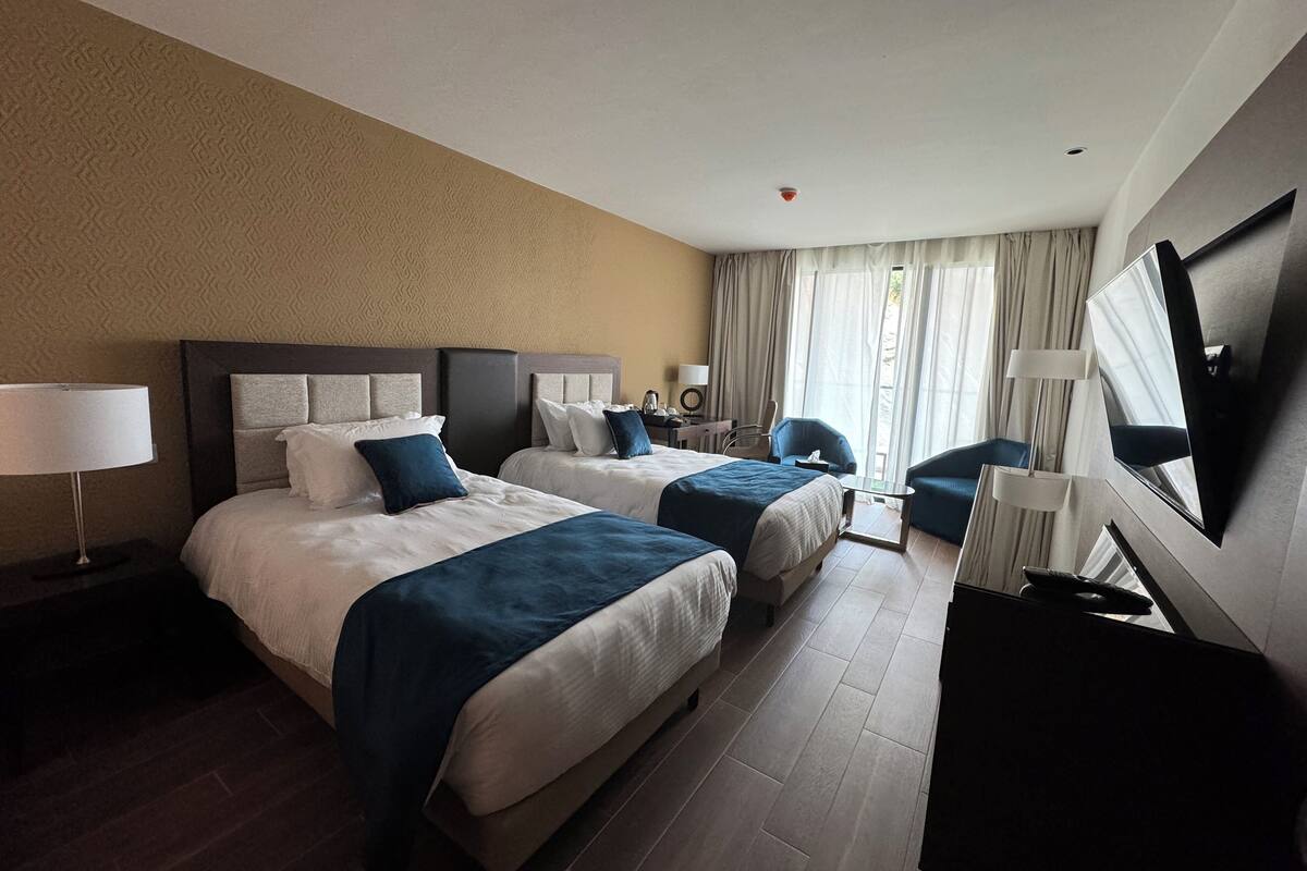 A hotel room with two beds, a desk, a chair, a TV, and a window with curtains.