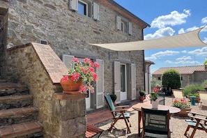 Un bâtiment en pierre doté d’un patio, de sièges en plein air et de plantes en pot.
